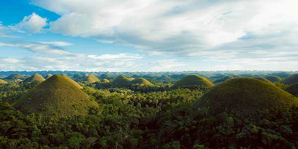 Scenic view of the Chocolate Hills in Bohol, Philippines, featuring rolling green hills under a clear blue sky.